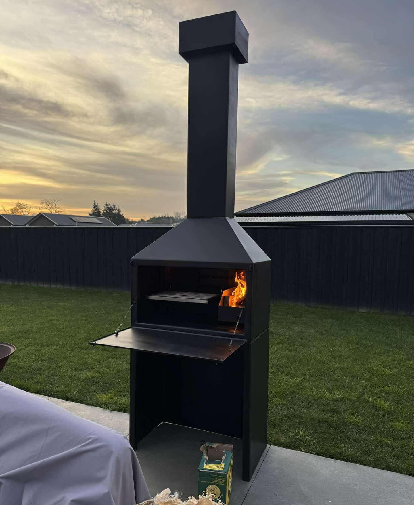 Tall Lotter outdoor fireplace burning at dusk